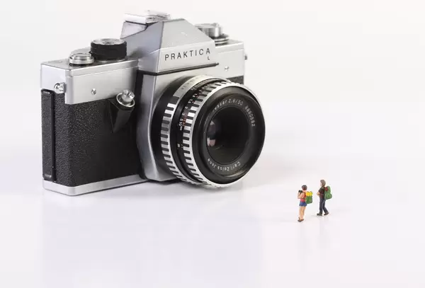 Miniature travelers with vintage camera on white background