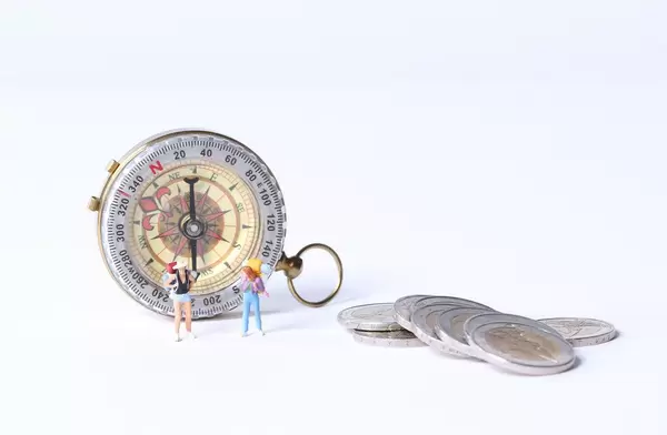 Miniature travelerswith coins and compas on white background