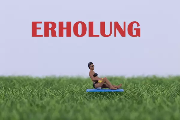 Miniature women relaxing on green grass eith Erholung text