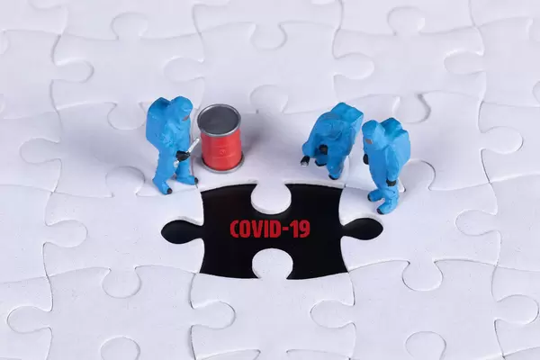 Miniature workers in chemical protection clothes with missing puzzle piece with Covid-19 text