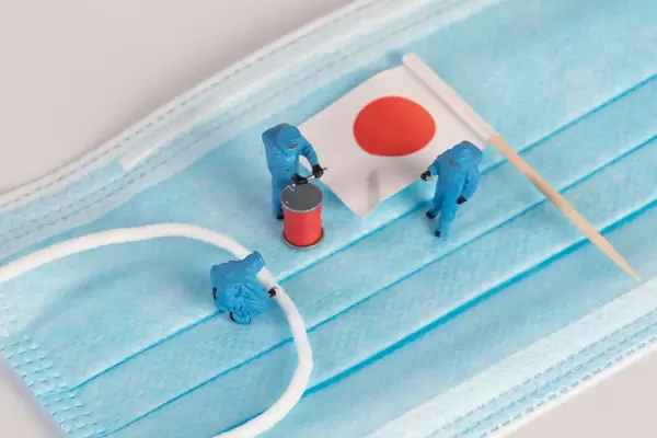 Miniature workers in protective clothes on a medical mask with flag of Japan