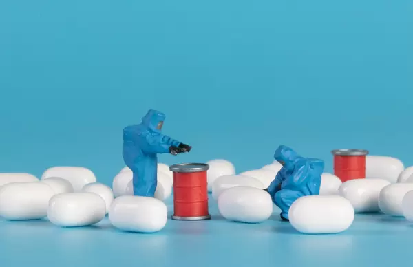 Miniature workers in protective clothes will pills on blue background