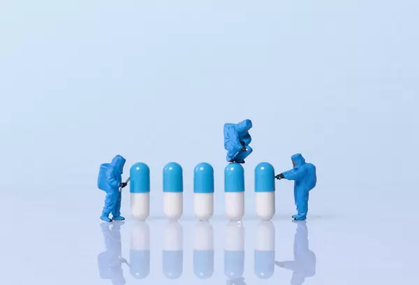 Miniature workers in safety uniforms and pills on light blue background