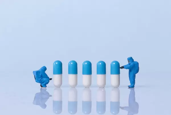 Miniature workers in safety uniforms with pills on light blue background