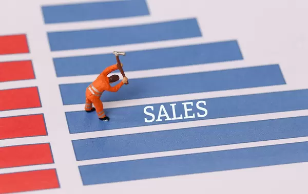 Miniature workers on a blue graph bar with Sales text