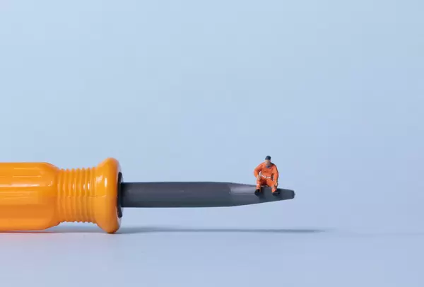Miniature workers sitting on a screwdriver