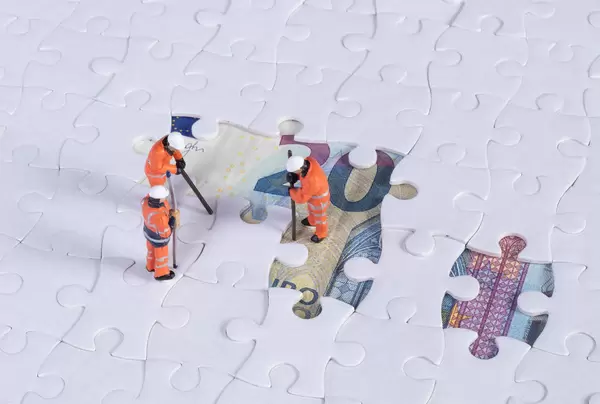 Miniature workers with missing jigsaw puzzle pieces on 20 Euro money banknote