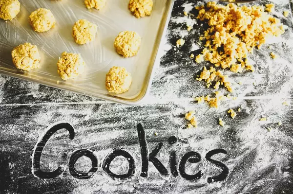 Mit dem Finger in Mehl geschriebenes Wort COOKIES vor noch ungebackenen Keksen und Plätzchenteig