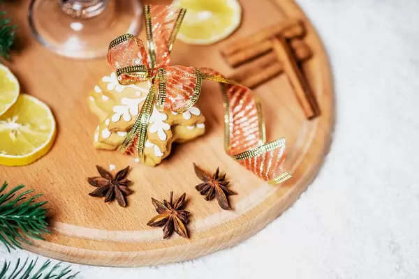 Mit einer Schleife gebundene Zimtsterne mit Zimt, Sternanis, einer Scheibe Zitrone und einem Glas Glühwein auf rundem Brettchen