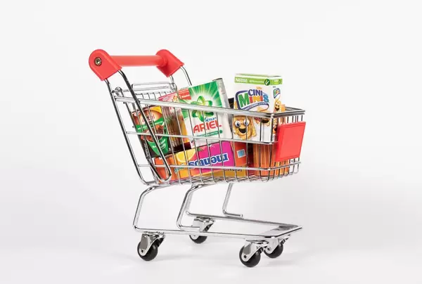 Mit Esswaren, Haushaltsprodukten und Süßwaren gefüllter Einkaufswagen vor weißem Hintergrund