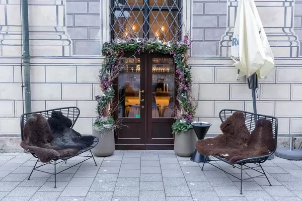 Mit Fell ausgestattete Sitzbänke vor mit Blumen dekortiertem Restauranteingang