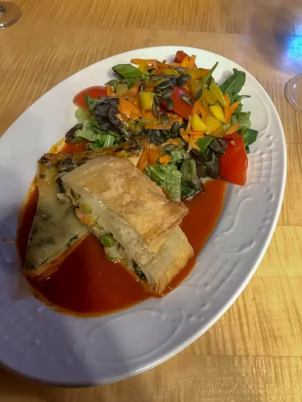 Mit Gemüse und Salat angerichtete Gemüselasagne in Tomatensoße auf Holztisch