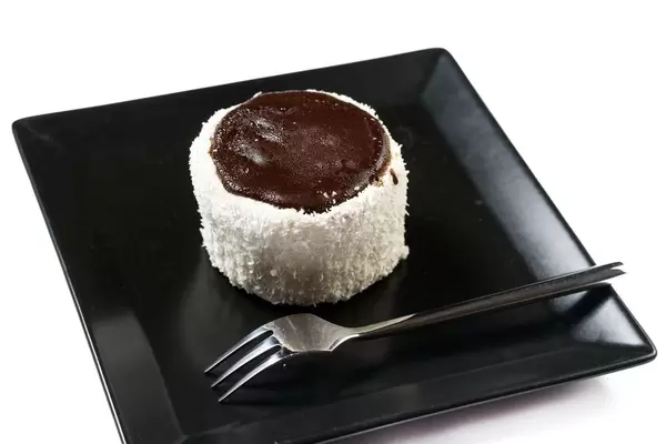 Mit Kokos und Schokolade verzierter Nachtisch mit liegender Gabel auf schwarzem Teller