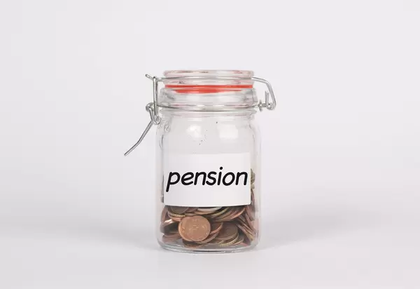 Mit Münzen gefülltes Glas mit Aufschrift PENSION symbolisiert Sparen für Rente