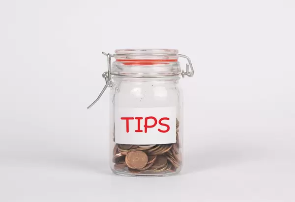 Mit Münzen gefülltes Glas mit roter Beschriftung TIPS (Trinkgeld) vor weißem Hintergrund