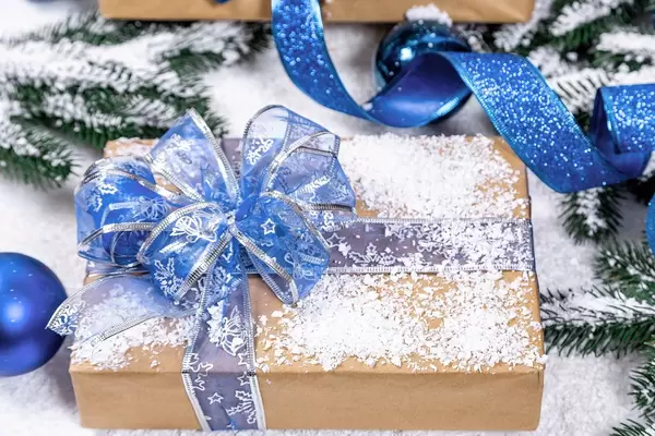 Mit Schnee berieseltes Geschenk in Naturpapier und Blauer Schleife