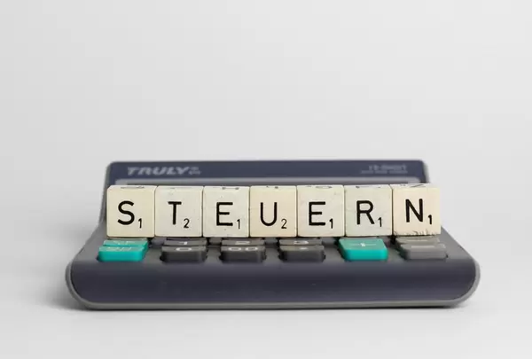 Mit Scrabble-Steinen gelegtes Wort 'Steuern' in zentraler Aufnahme auf elektronischen Taschenrechner