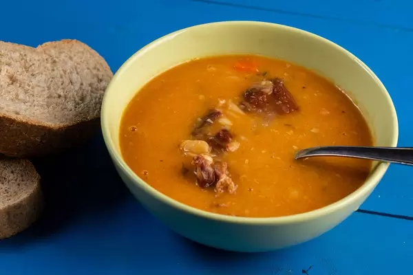 MIttagessen mit gekochten Bohnen, Schweinefleisch und Weißbrot auf einem blauen Holztisch