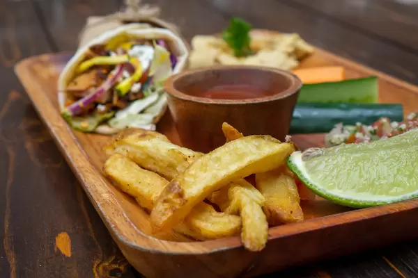 Mittagessen Set auf einem Holzbrett bestehend aus Döner Dürum Wrap mit Hähnchenfleisch, Pommes Frites, Hummus, Quinoa Salat und Gemüse Nahaufnahme