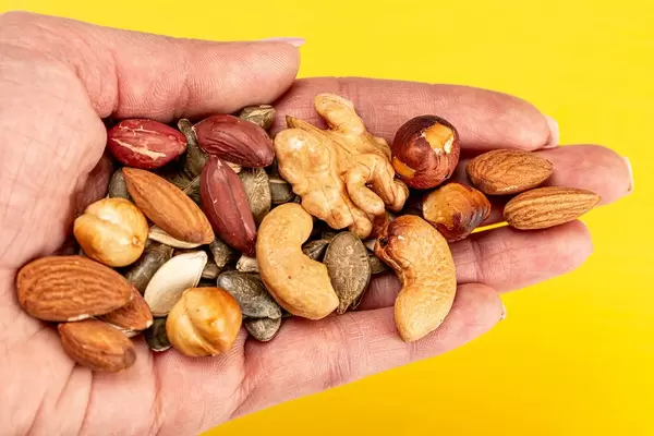 Mix nuts and seeds in a female hand on a yellow background