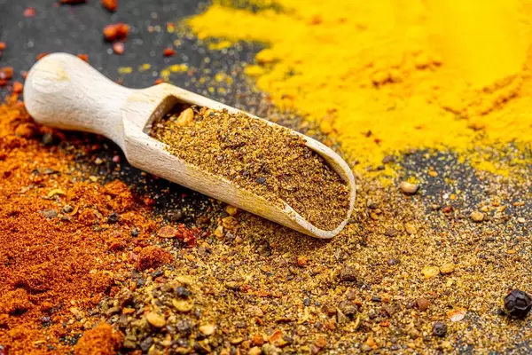 Mix of peppers in a wooden scoop on a background of ground spices