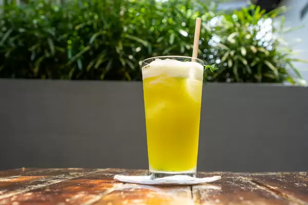 Mixed Fruit Juice with Passion Fruit, Pineapple and Yuzu in a Glass with Paper Straw and Rosemary on a Fabric Saucer with Plants in the Background