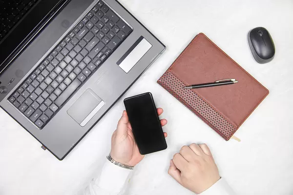 Mobile phone in the hand of a businessman in front of a laptop