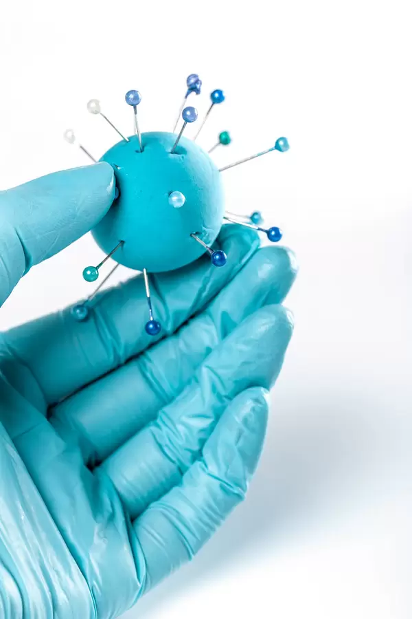 Model of coronavirus or other virus made from plasticine and pins in hand with glove