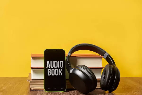 Modern wireless headphones with hardcover books and smartphone against the yellow colored background