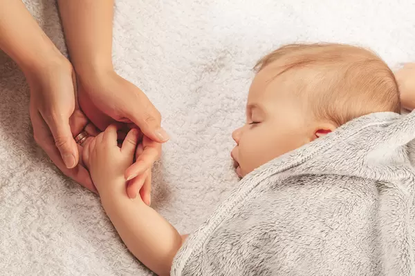 Mom holds the hand of her little sleeping child