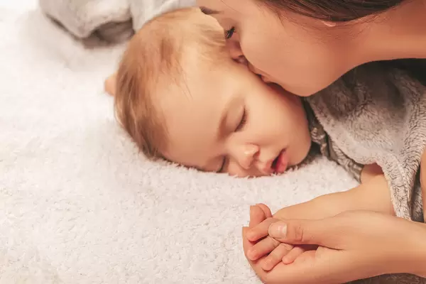 Mom kisses her little sleeping child on the cheek