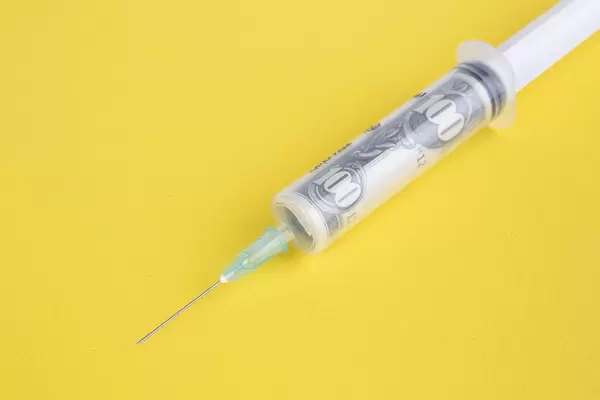Money in syringe on yellow background
