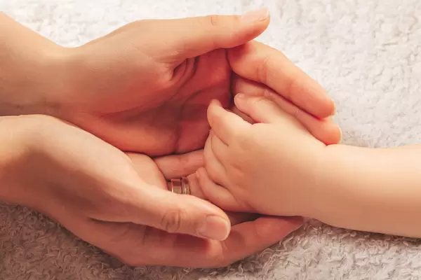 Mother hands hold her baby's tiny hand. Concept love, warm and secure