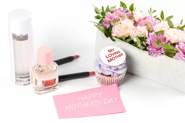 Mothers day greeting background with perfumes, lipsticks, flowers and cupcake