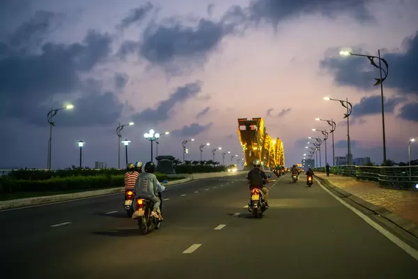Motorbikes driving towards the Dragon Head of the iconic Dragon Bridge with Colorful Sky in the Evening in Da Nang, Vietnam