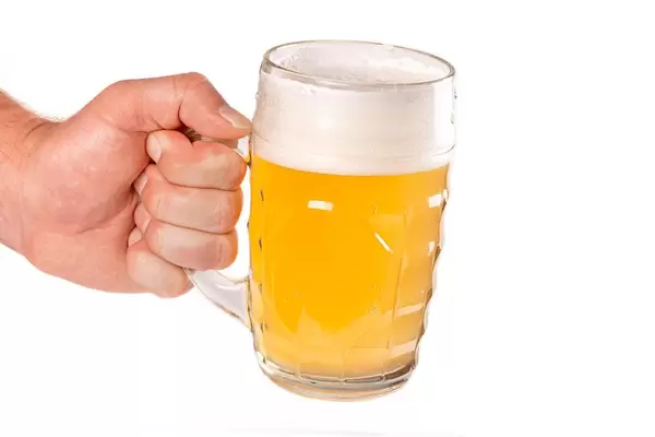 Mug of unfiltered light beer with foam in a man's hand