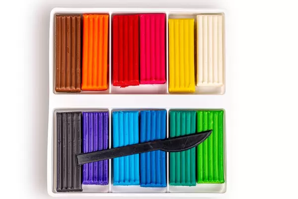 Multi-colored plasticine with a plastic knife in a box on white, top view