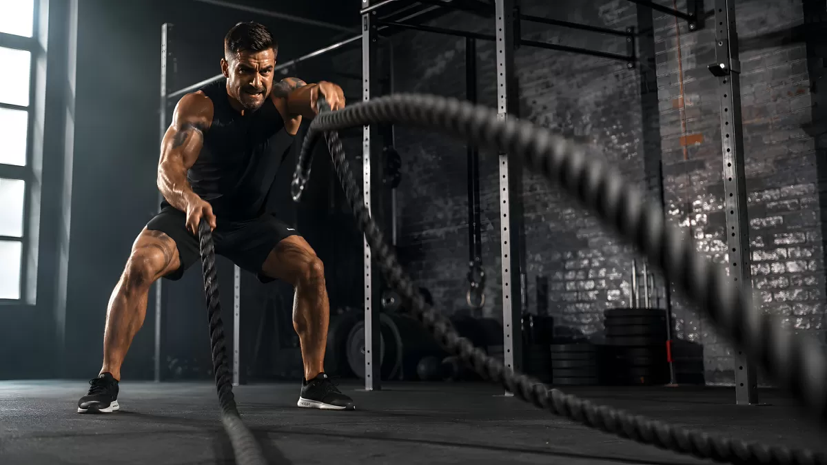 Muskulöser Athlet trainiert mit Battle Ropes im Gym