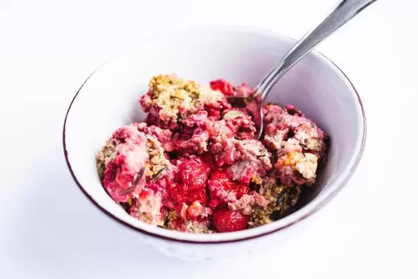 Müsli mit Kürbiskernen und Erdbeeren in einer Schüssel und einem Löffel auf weißem Hintergrund