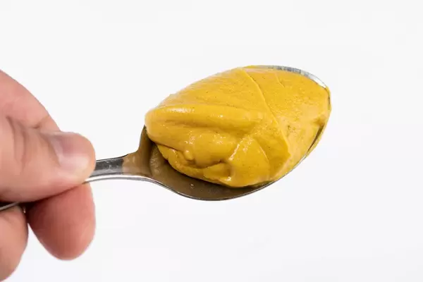 Mustard on the spoon above white background