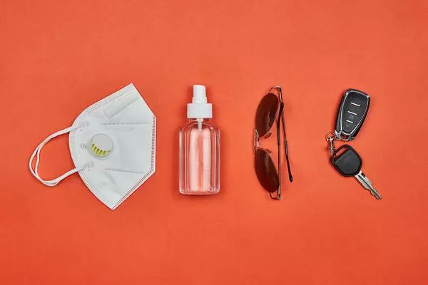 N95 face mask, disinfectant bottle, sunglasses and car keys on red background
