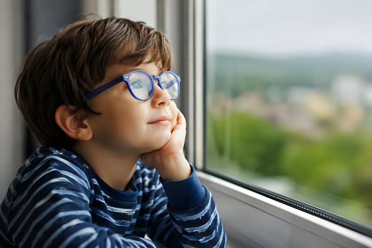 Nachdenklicher Junge mit Brille schaut aus dem Fenster