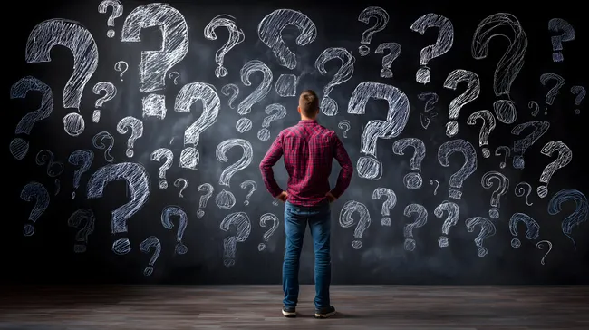 Nachdenklicher Mann vor Kreidetafel mit Fragezeichen