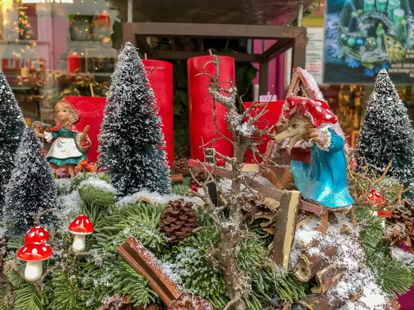 Nachstellung des Märchens Rotkäppchen, Wolf schleicht sich als Großmutter verkleidet an Rotkäppchen, die im verschneiten Wald zwischen Tannenbäumen und Pilzen steht, im Hintergrund vier rote Kerzen und Weihnachtsdekoration in Schaufenster