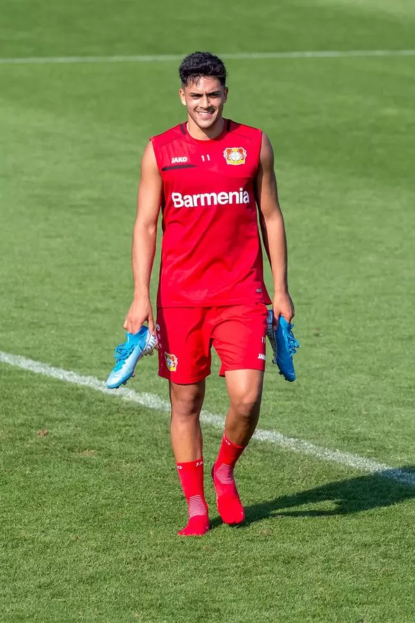 Nadiem Amiri in rotem Barmenia-Fußballtrikot, trägt seine blauen Fußballschuhe in den Händen