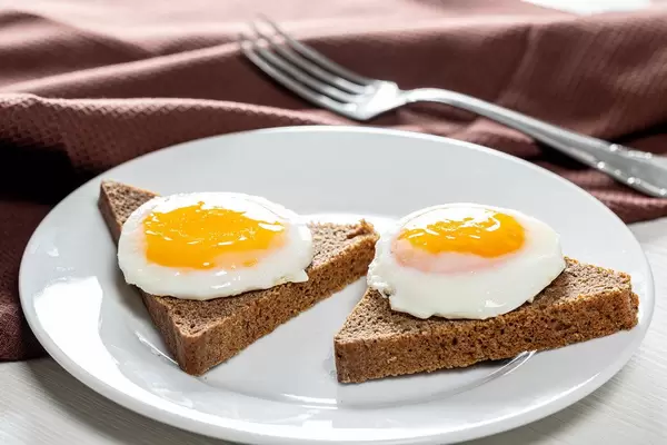 Nahaufnahme auf Frühstücksteller mit zwei akkurat geformten Spiegeleiern auf Toast