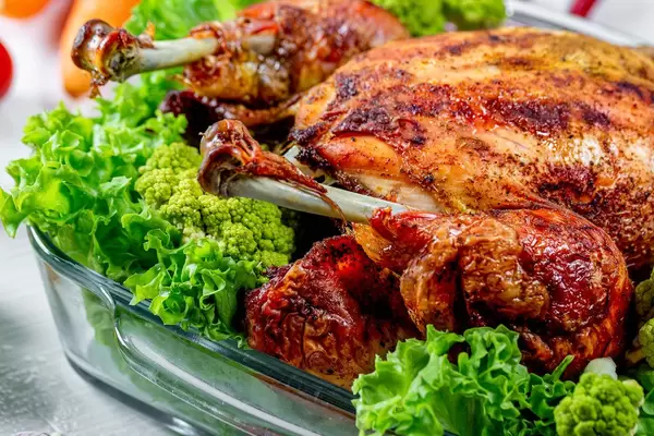 Nahaufnahme auf knusprig gebratenes ganzes Hähnchen mit Brokkoli und Blattsalat in Glasschale