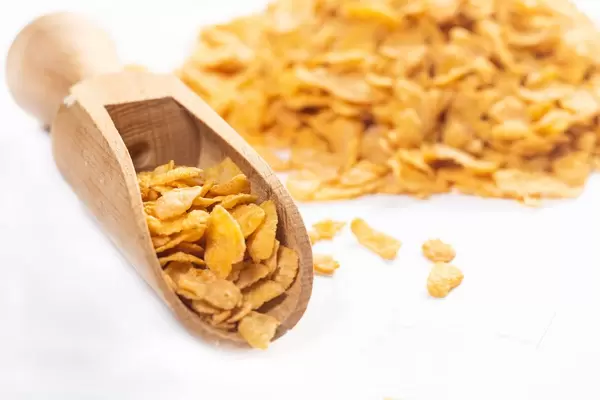 Nahaufnahme Cornflakes in hölzerner Schaufel vor Haufen mit Cornflakes mit Schärfentiefe
