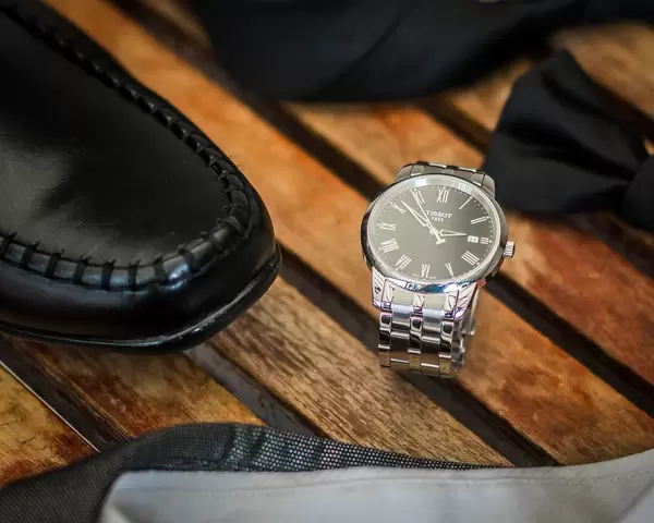 Nahaufnahme der Accessoires des Bräutigams wie luxuriöse Uhr und elegante Lederschuhe auf Holz