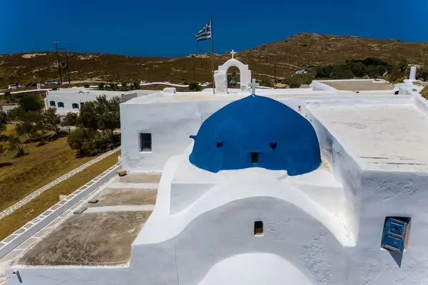 Nahaufnahme des blauen Kuppeldachs des Klosters von Agios Ioannis Detis, mit wehender Griechenlandfahne im Hintergrund